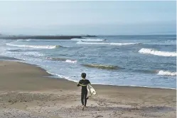  ?? JAE C. HONG/ASSOCIATED PRESS ?? A young surfer walks Wednesday along Tsurigasak­i beach, a venue for surfing at the Tokyo 2020 Olympics, in Ichinomiya, Chiba prefecture, east of Tokyo. As one of five new sports being added to the program for 2020 Tokyo Olympics, surfing is arguably the most glamorous and is sure to bring a new dimension as the IOC seeks a younger audience.