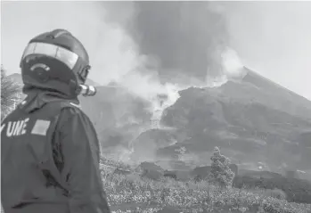  ?? LUISMI ORTIZ/UME ?? A member of the Spanish Military Emergency Unit (UME) monitors the Cumbre Vieja volcano on Saturday as a new river of lava flowed from the volcano on the Canary island of La Palma. Over 1,000 buildings have already been damaged by lava since the volcano’s initial Sept. 19 eruption and thousands of people evacuated.