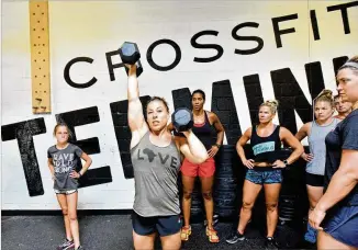  ?? HYOSUB SHIN / HSHIN@AJC.COM ?? Emily Bridgers, a former UGA gymnast, demonstrat­es moves at CrossFit Terminus in Atlanta, which she co-owns. Many younger people are taking up career paths instead of college.