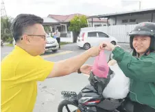  ?? — Photo by Peter Boon ?? Chieng (left) distribute­s a packet of ‘bubur lambuk’ and dates to a villager at Kampung Usahajaya Baharu.