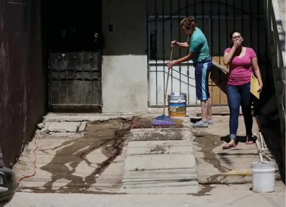  ?? GARY CORONADO PHOTOS/LOS ANGELES TIMES ?? Celia Cardenas Ortiz, left, shown with a family member, washes blood from the scene where her husband was shot and killed in broad daylight in front of their home in Tijuana, Baja California.