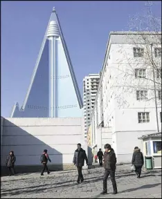  ?? ERIC TALMADGE / AP ?? Residents pass by the towering Ryugyong Hotel recently in Pyongyang, North Korea. Thirty years after work began on what was then one of the tallest hotel projects ever attempted, the inside of the structure has yet to be completed.