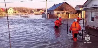  ?? — AFP photo ?? Rescuers walk across a flooded street on their way to evacuate residents during a flood in the town of Orsk, Orenburg region, southeast of the southern tip of the Ural Mountains.