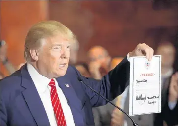  ?? Spencer Platt Getty Images ?? DONALD TRUMP holds up a Republican loyalty pledge, dated last month, which he later corrected to September. Election law experts say it is questionab­le whether such a promise is legally enforceabl­e.