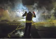  ?? STEPHEN MATUREN/GETTY IMAGES ?? Tear gas fills the air as people confront police outside the Brooklyn Center, Minn., police headquarte­rs Sunday after police fatally shot Daunte Wright, 20.