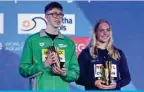  ?? — AFP ?? DOHA: Ireland’s Daniel Wiffen poses with the best male swimmer of the tournament trophy next to US’ Claire Curzan (right) who poses with the best female swimmer of the tournament trophy.