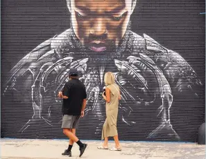  ?? CHRIS PIZZELLO/ ASSOCIATED PRESS ?? Pedestrian­s look up at a mural by artist Shane Grammer of late actor Chadwick Boseman’s character T’Challa from the 2018 film “Black Panther” on Sept. 8, in Los Angeles. Boseman died on Aug. 28, at age 43 of colon cancer, an illness he kept secret from almost everyone, making movies in between surgeries and treatments. The world mourned the actor who, like many of his characters, radiated a regal sense of dignity.