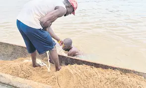  ?? ?? Saturnin Yenzia (left) pulls a rope to get a bucket of sandf onto his pirogue on the Ubangi river in Bangui.