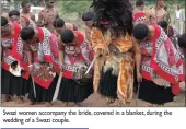  ??  ?? Swazi women accompany the bride, covered in a blanket, during the wedding of a Swazi couple.