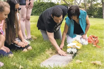  ??  ?? From left, Andrew Romero comforts his grandmothe­r Debbie Romero as they clean his father’s grave following a Fiesta de Santa Fe procession on Sunday.