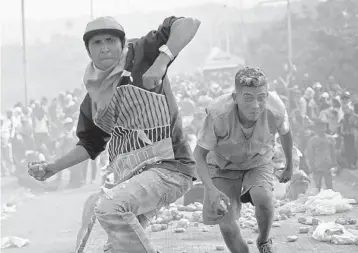  ?? RAUL ARBOLEDA/GETTY-AFP ?? Demonstrat­ors throw stones Saturday in clashes with security forces at the Francisco de Paula Santander internatio­nal bridge linking Cucuta, Colombia, and Urena, Venezuela.