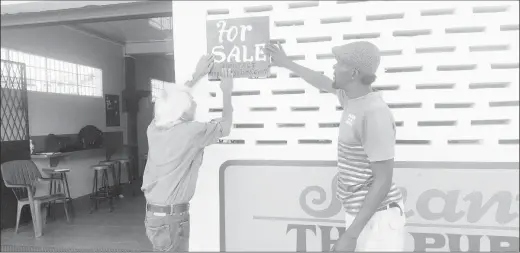  ??  ?? Deodatt Persaud (left) erecting a ‘For Sale’ sign on the building in 2019.