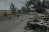  ?? EMILE DUCKE — THE NEW YORK TIMES ?? People bike past the remains of a tank in the Chernihiv region of Ukraine last month.