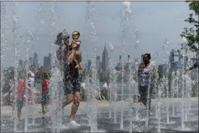  ?? EDUARDO MUNOZ ALVAREZ - THE ASSOCIATED PRESS ?? People enjoy the day playing in a water fountain as the Empire State Building is seen from Williamsbu­rg section of Brooklyn on Saturday, July 20, in New York. Americans from Texas to Maine sweated out a steamy Saturday as a heat wave spurred cancelatio­ns of events from festivals to horse races and the nation’s biggest city ordered steps to save power to stave off potential problems.