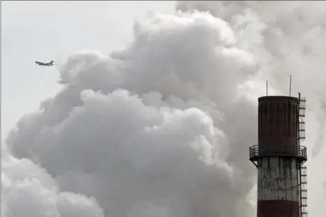  ?? ANDY WONG — THE ASSOCIATED PRESS FILE ?? A passenger airplane flies behind steam and white smoke emitted from a coal-fired power plant in Beijing.