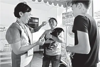  ?? MACKY LIM ?? ANTI-RABIES SHOT. A pet owner tightly holds her dog and calms it as an employee of the Davao City Veterinari­an's Office prepares to administer an anti-rabies shot after the dog squeezes its way out away from the syringe.