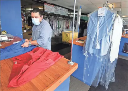  ?? RICK WOOD / MILWAUKEE JOURNAL SENTINEL ?? Prestige Dry Cleaners owner Oscar Marin fills an order Friday. He closed the business in March, both because of the threat of the virus and pretty much no demand for dry cleaning, and opened back up toward the end of May. Business isn’t quite back to normal, but he keeps his employees feeling safe amid the pandemic (especially since they’re handling dirty laundry) by requiring masks for the people who come in, disinfecti­ng everything and installing UV lights and plexiglass shields where customers come into contact with employees.