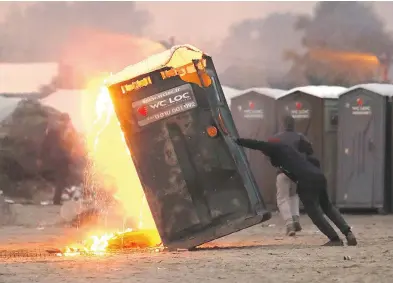  ?? CHRISTOPHE­R FURLONG / GETTY IMAGES ?? A migrant sets fire to a chemical toilet inside “the jungle” camp Monday in Calais, France. Many migrants have left by bus to be relocated at centres across France as police and officials begin to clear the unofficial camp.