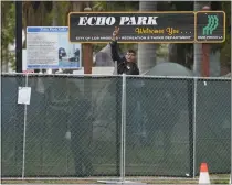  ?? DAMIAN DOVARGANES – THE ASSOCIATED PRESS ?? A homeless activist makes a peace sign gesture over a fence as Los Angeles sanitation workers move inside the closed perimeter of Echo Park Lake on March 25, 2021. The fence is about to come back down.