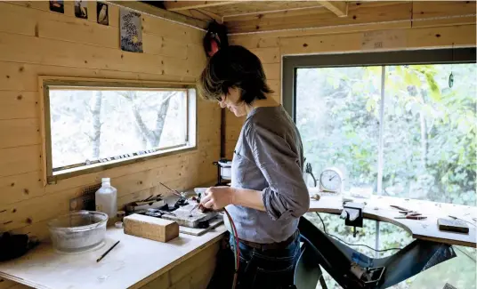  ??  ?? Laura Brown, amid the trees in the peace of her workshop, soldering layers of a silver woodland scene to make one of her unusual 3D pendants.