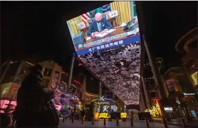  ?? (AP/Mark Schiefelbe­in) ?? A vendor selling lighted balloons stands Thursday near a large video at a shopping mall in Beijing showing a government news report about the inaugurati­on of President Joe Biden.