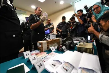  ??  ?? Mustafar (left) shows the false identifica­tion documents seized to the media. — Bernama photo