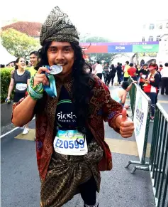  ??  ?? A participan­t, dressed in traditiona­l Malay costume, bites his Kuching Marathon finisher’s medal as he poses for photograph­s.