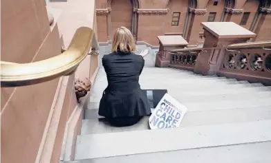  ?? CINDY SCHULTZ/THE NEW YORK TIMES ?? A woman sits at the state Capitol in Albany, New York, alongside a sign calling for universal child care.