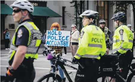  ??  ?? A protester holds a sign as police keep watch on thousands of people demonstrat­ing against racism and police brutality, in Vancouver on May 31. The peaceful demonstrat­ion was held in the wake of the deaths of George Floyd in the U.S. and Regis Korchinski-Paquet in Toronto.