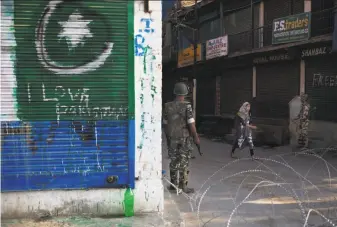  ?? Dar Yasin / Associated Press ?? A Kashmiri girl walks past Indian paramilita­ry soldiers near a temporary checkpoint in Srinagar in Indian-controlled Kashmir, where graffiti supporting Pakistan is painted on a wall.