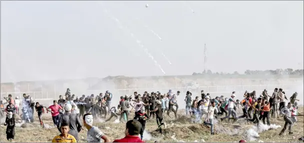  ??  ?? Palestinia­n men take cover from tear gas shot by Israeli forces during a demonstrat­ion along the border with the Gaza strip. — AFP photo