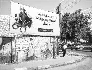  ??  ?? A man walking past a banner carrying the writing in Arabic ‘we declare our full support for the security authoritie­s in their measures against collaborat­ors’ and ‘they betrayed, and backstabbe­d, and deserved the punishment’, describing people suspected of working for Israel. — AFP photo