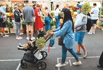  ?? AFP ?? A woman pushes a pram along the street as people queue to buy flowers and plants at Columbia Road flower market in east London yesterday.