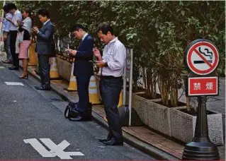  ??  ?? Clockwise from top left: People smoke in a designated smoking area in Tokyo; A sign welcomes smokers to a restaurant in Tokyo; People smoke and vape next to a no smoking sign in Tokyo; Activists rally behind a banner noting that smoking on the street...