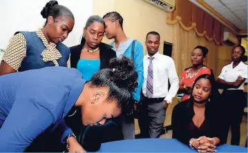  ?? RUDOLPH BROWN/ PHOTOGRAPH­ER ?? Serena Lawrence (left) signs her name while other students look on at the Jamaica Social Investment Fund Poverty Reduction Programme Tertiary Scholarshi­ps Recognitio­n Ceremony at the UWI Visitors’ Lodge, UWI Mona campus, on Friday, March 2.