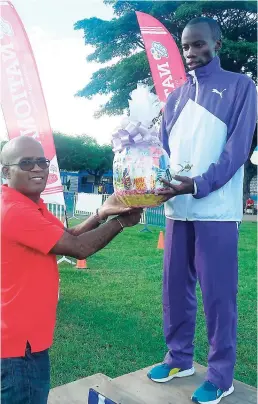  ??  ?? Ari Rodgers (right) of Kingston College, winner of the men’s 5K at the Hugo Chambers Memorial Road Race, receiving a gift basket from Roan Wong, vice-principal of Jamaica College.