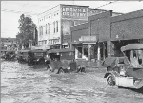  ?? Photo courtesy of the North Little Rock History Commission ?? Vehicles plow through the water in the 100 block of North Maple Street in North Little Rock, where much of the downtown area was inundated in the 1927 flood.