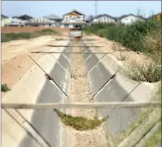  ?? AP photo ?? A dry irrigation canal runs between two unplanted fields as new home constructi­on abuts dormant fields owned by Kelly Anderson on Thursday, in Maricopa, Ariz. Anderson grows specialty crops for the flower industry and leases land to alfalfa farmers whose crops feed cattle at nearby dairy farms. He knows what’s at stake as states dither over cuts and expects about half of the area will go unplanted next year, after farmers in the region lose all access to the river.