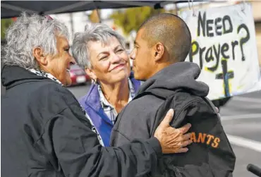  ??  ?? Ivan Mendoza, who was riding his bike when he stopped for a prayer, listens as Virginia La Salle, left, and Linda Crowder, center, chat with him at a pair of canopies set up for free prayers.