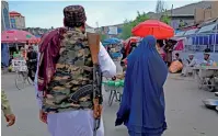  ?? ?? A woman wearing A Burqa walks through A market As A TALIBAN fighter stands GUARD In Downtown KABUL. — ap