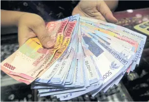  ?? EPA ?? An Indonesian vendor holds rupiah notes at a market in Jakarta. Indonesia’s economy grew 4.73% in the third quarter, higher than the second quarter’s growth of 4.6%, the Central Statistics Agency reported.