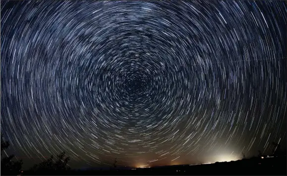  ?? COURTESY MAURICE ROETHEL ASTROPHOTO­GRAPHY ?? This image was taken Oct. 28 in Sandia Park, N.M. It helps us visualize the earth’s axis with motion around it. Here we see a time exposure taken from a camera on a fixed mount pointed toward true north. Each arc of blue, white or red light represents a single star smeared out by the rotation of the earth during several minutes of exposure. Polaris, the North Star, is the little bright smudge nearest the center of this cosmic maelstrom. Lights along the bottom right are from Santa Fe. There is a faint almost horizontal line going across the star trails. If you zoom in, you’ll see the red and green wingtip lights from a passing airplane. There is also one short bright streak near the glow of the ground lights that’s not in line with the star trails. That streak is a meteor.