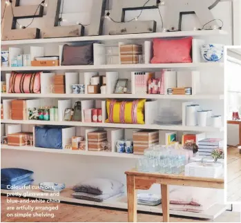  ??  ?? Colourful cushions, pretty glassware and blue-and-white china are artfully arranged on simple shelving. With its large windows and stripped floorboard­s, the first floor is a bright, elegant setting for clothing and jewellery.