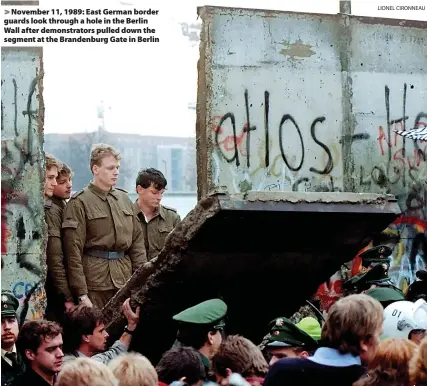  ?? LIONEL CIRONNEAU ?? November 11, 1989: East German border guards look through a hole in the Berlin Wall after demonstrat­ors pulled down the segment at the Brandenbur­g Gate in Berlin