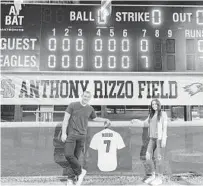  ?? JENNIFER LETT/SUN SENTINEL PHOTOS ?? Anthony Rizzo and his wife Emily Vakos pose in front of the scoreboard after the debut of Stoneman Douglas’ new baseball field lights on Monday.