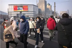  ?? (AP Photo/Mark Schiefelbe­in) ?? Commuters wearing face masks walk across an intersecti­on near an electronic billboard for China’s armed forces during the morning rush hour Friday in Beijing.