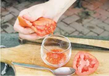  ?? Lee Reich / Associated Press ?? Cutting a tomato in half and squeezing the seeds into a glass or a jar is the first step to having your home-grown seeds for next year's tomatoes.