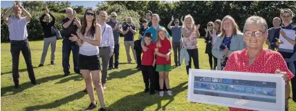  ??  ?? Pat Anthony, sister of the late Kevin Stonehouse, with a framed copy of the mural, at the unveiling ceremony. Included in the picture is Tre Cwm estate’s artist-in-residence Kristin Luke, fourth left