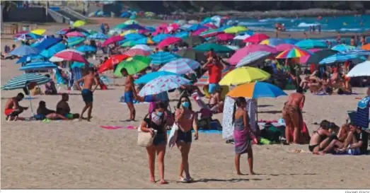  ?? ERASMO FENOY. ?? Dos personas con mascarilla en la playa de El Rinconcill­o.