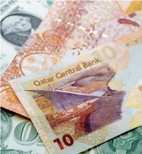  ?? — Bloomberg ?? A Qatari Riyal bank note sits with a US Dollar note. Many Qatari shares are now trading at or above fair value, leaving the market vulnerable to a correction